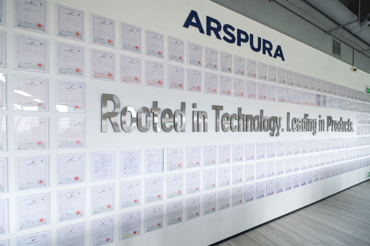 Arspura patent display wall with rows of framed certificates, ARSPURA lettering above, and the slogan “Rooted in Technology. Leading in Products.” in metallic letters.