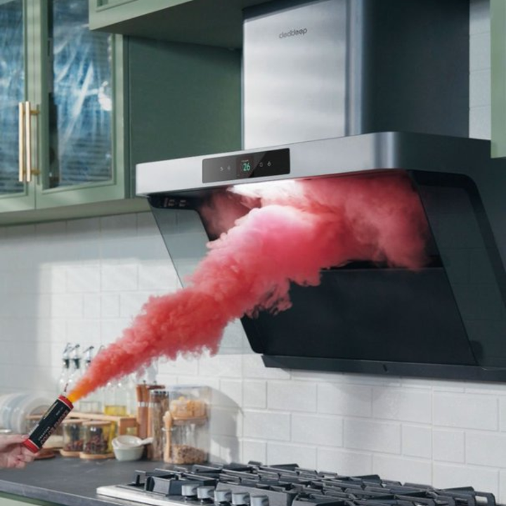 Stainless steel range hood capturing a vivid red smoke plume in a kitchen, demonstrating strong suction and wide capture area