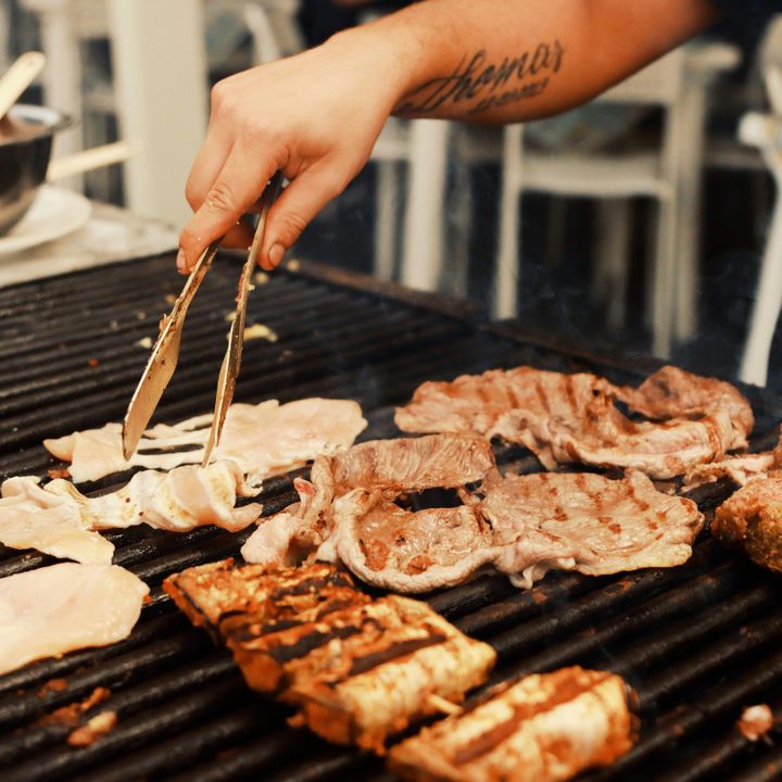 Various meats grilling on a large indoor cooktop, creating significant smoke and steam that require a high-performance range hood for ventilation