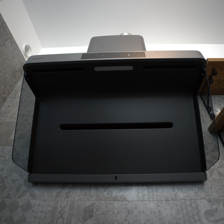 A bottom-up view of a modern range hood, showcasing its large black capture area, slim horizontal vents, and protective glass side panels