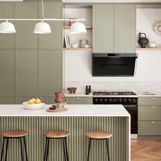 Contemporary kitchen island with white waterfall countertop, wooden bar stools, sage green fluted cabinetry, and black angled range hood above gas range