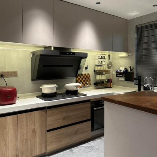 Angled black wall-mount range hood installed in contemporary L-shaped kitchen with wood-tone cabinets and under-cabinet lighting