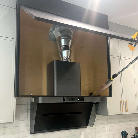 Black wall-mount range hood with rigid metal ductwork and 90-degree elbow installed above professional gas cooktop in white kitchen