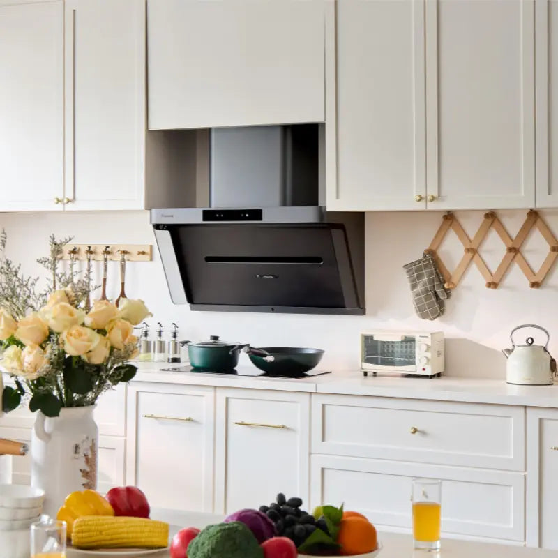 Modern black angled range hood installed in a white kitchen with fresh flowers and colorful produce in the foreground