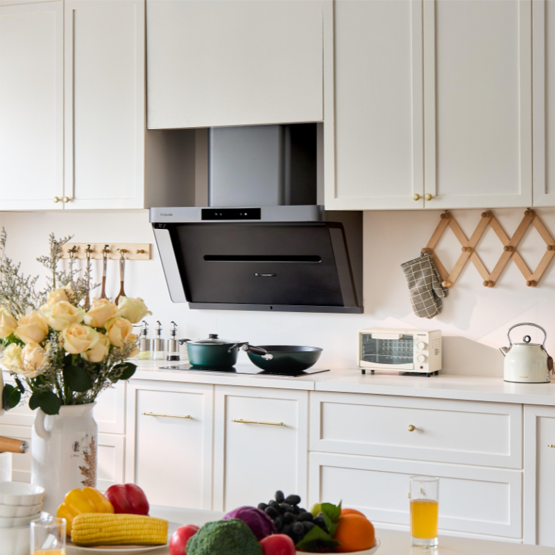 Modern black angled range hood installed in a white kitchen with fresh flowers and colorful produce in the foreground